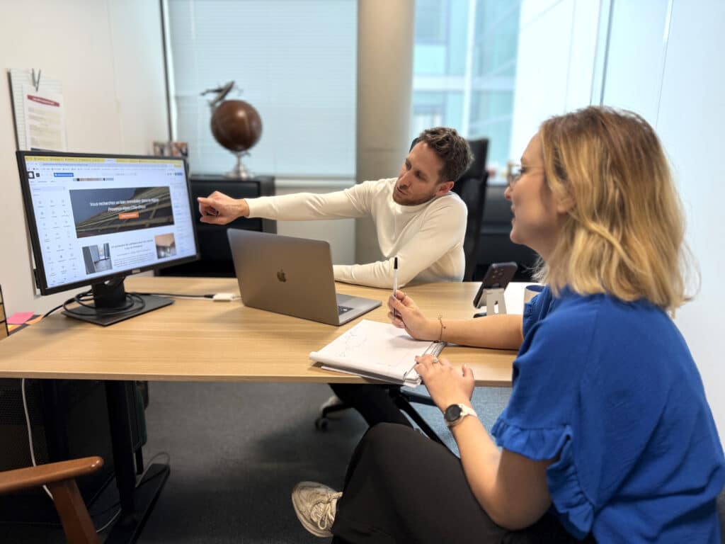 Développement web : Collaboration sur un projet immobilier Collaboration en bureau. L'homme pointe l'écran de design web affichant "Vous recherchez un bien immobilier dans la région Provence-Alpes-Côte-d'Azur".