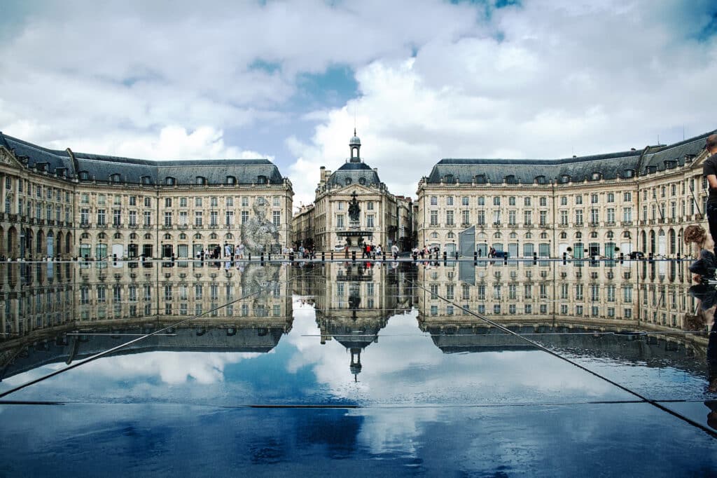 Miroir d'eau Bordeaux : Reflets parfaits de la Place de la Bourse. Architecture de la Place de la Bourse de Bordeaux reflétée dans le Miroir d'eau, sous un ciel nuageux.