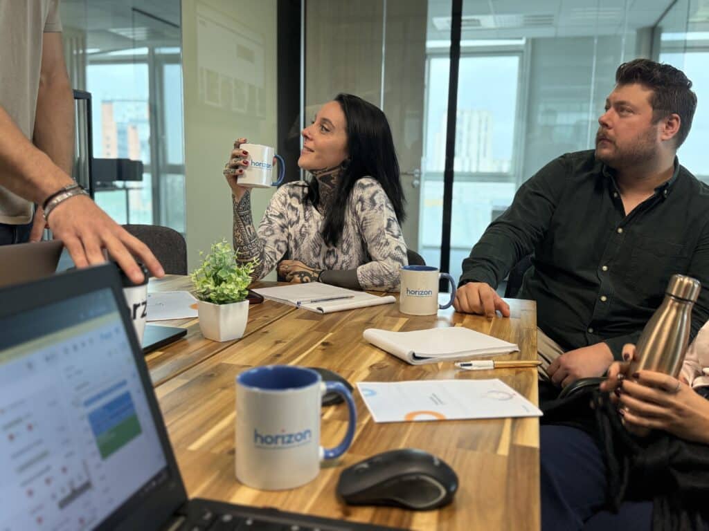 Réunion de travail agence web Horizon Réunion d'équipe collaborative au bureau. Des professionnels discutent autour d'une table, avec des mugs « horizon création & référencement de sites web ».