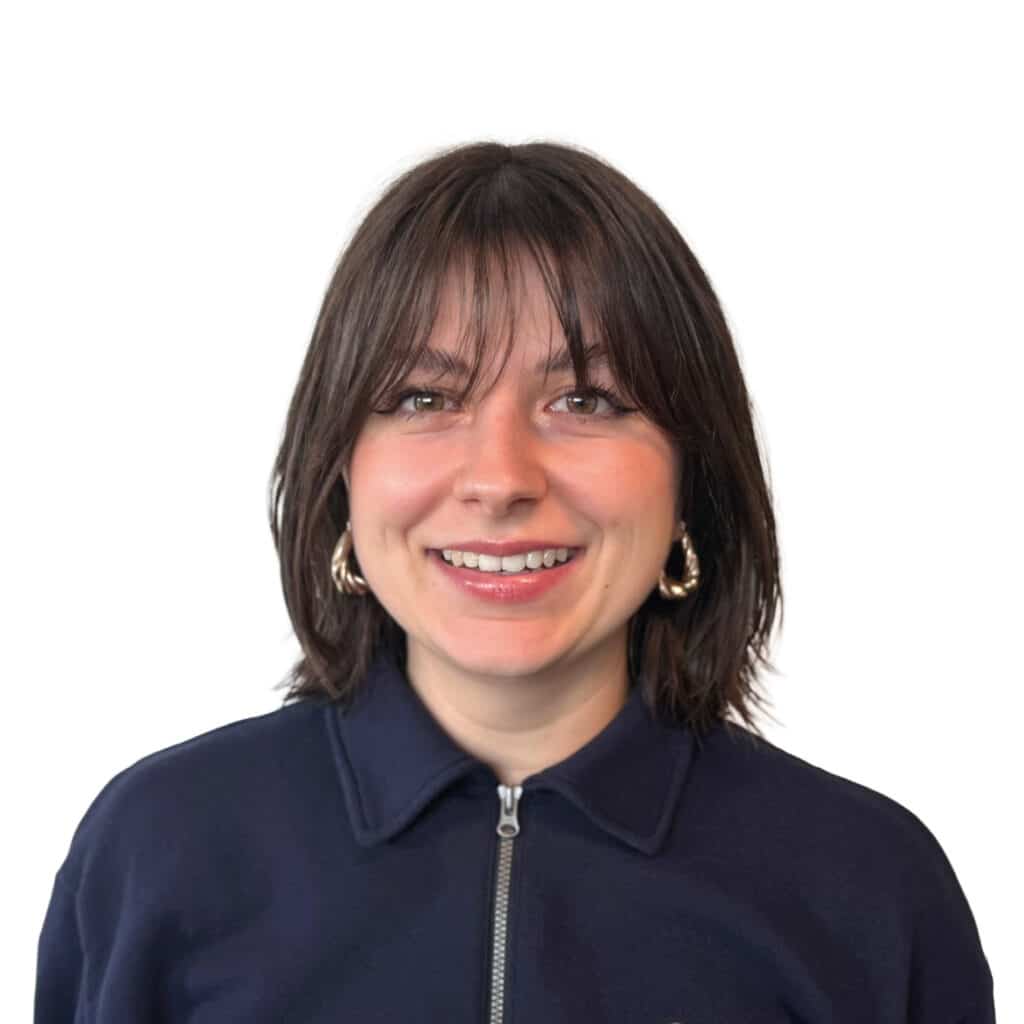 Femme souriante aux cheveux bruns et frange en pull marine Femme souriante aux cheveux bruns et frange, portant un pull bleu marine et des créoles dorées sur fond blanc.