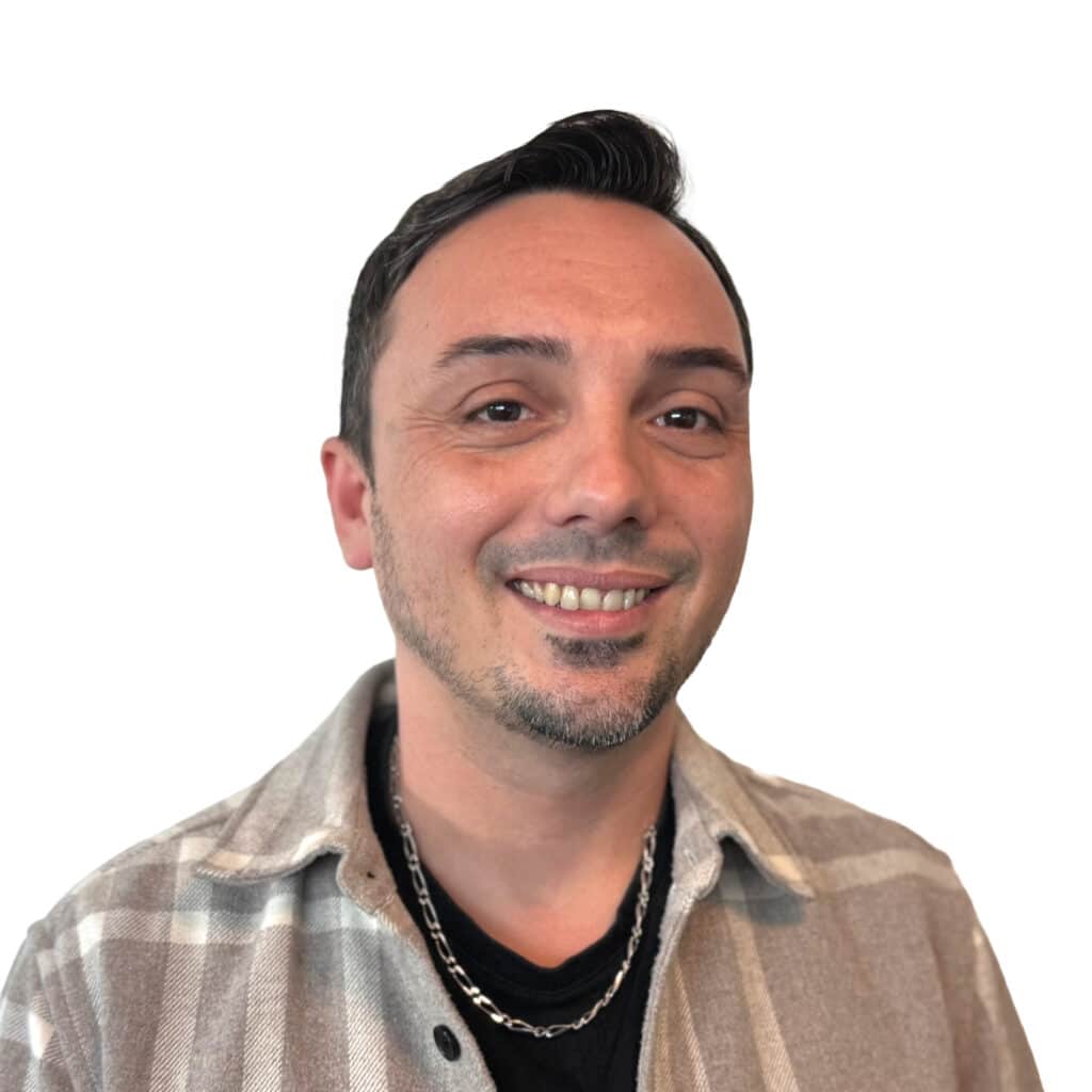 Portrait d'un homme souriant en chemise à carreaux beige Homme souriant avec barbichette, vêtu d'une chemise à carreaux beige et d'une chaîne argentée sur fond blanc.