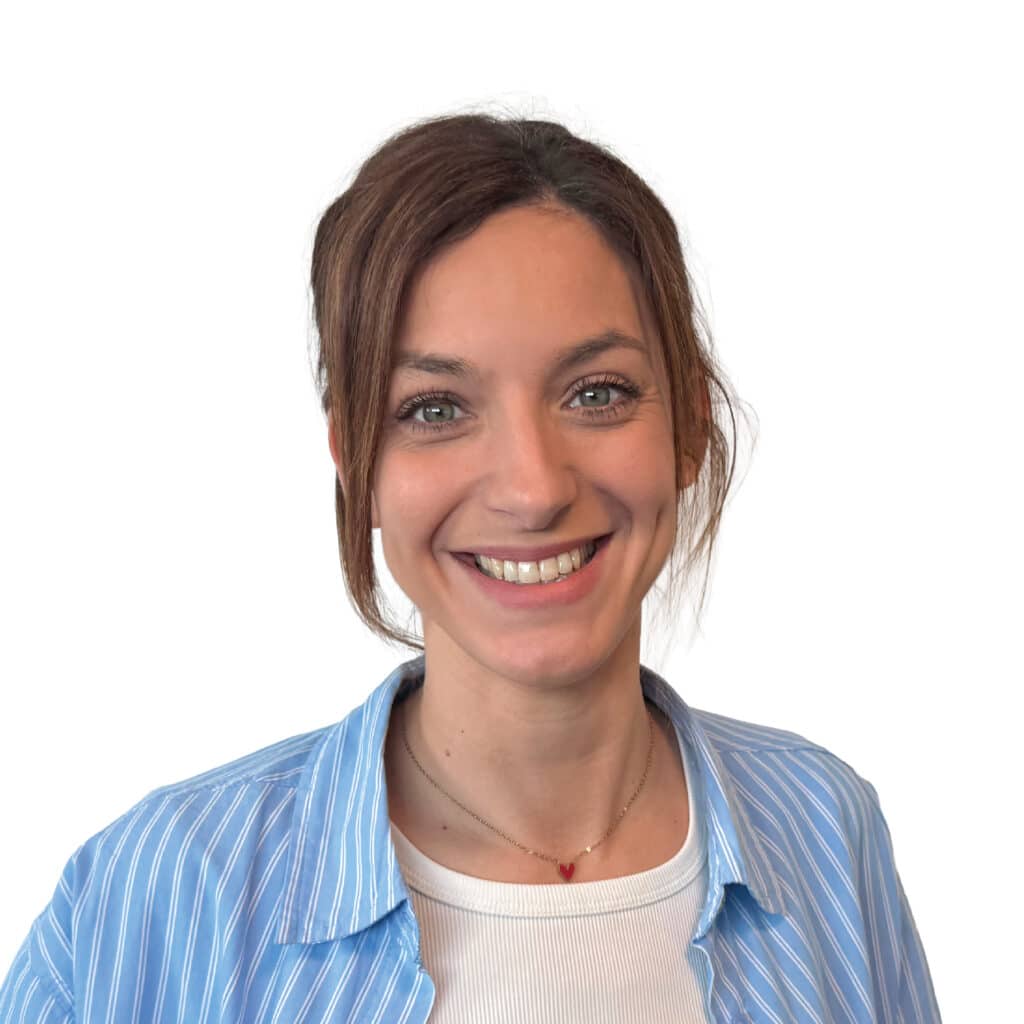 Portrait d'une femme souriante en chemise bleue rayée Femme souriante aux yeux verts, portant une chemise rayée bleue et un collier cœur rouge sur fond blanc.